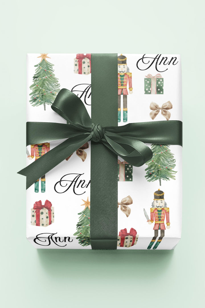 wrapping paper with white background and graphics of a nutcracker, christmas tree, christmas present, bow, and script text with a personalized name