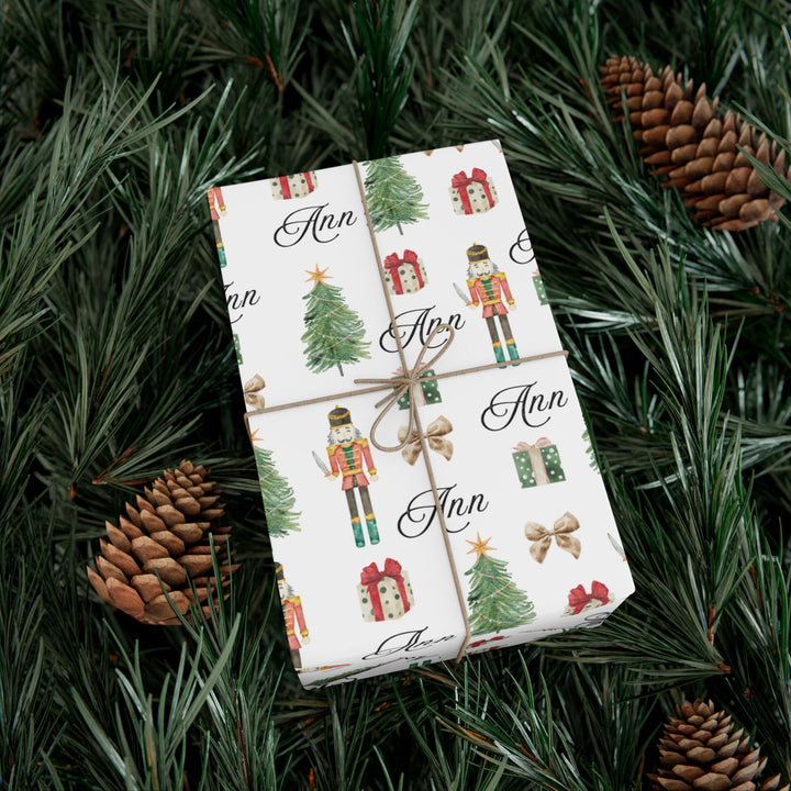 wrapping paper with white background and graphics of a nutcracker, christmas tree, christmas present, bow, and script text with a personalized name