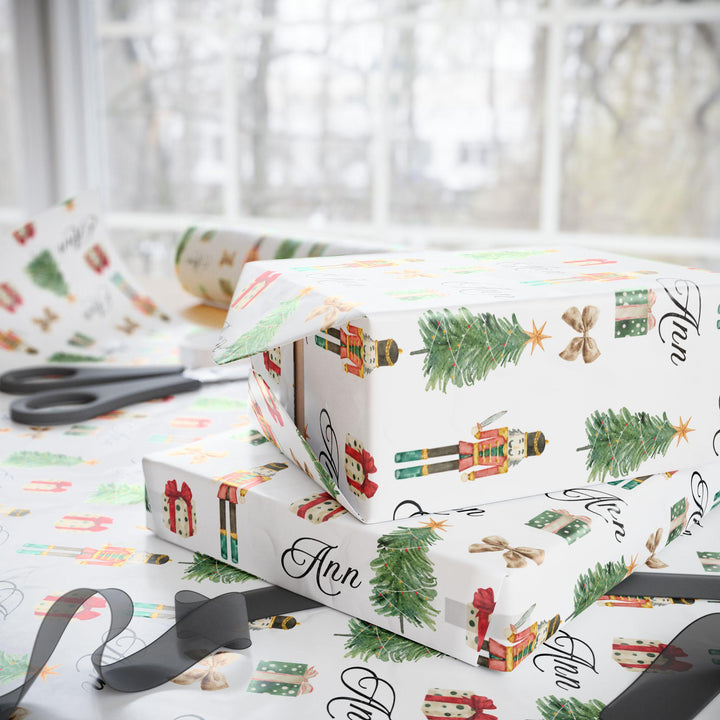 wrapping paper with white background and graphics of a nutcracker, christmas tree, christmas present, bow, and script text with a personalized name