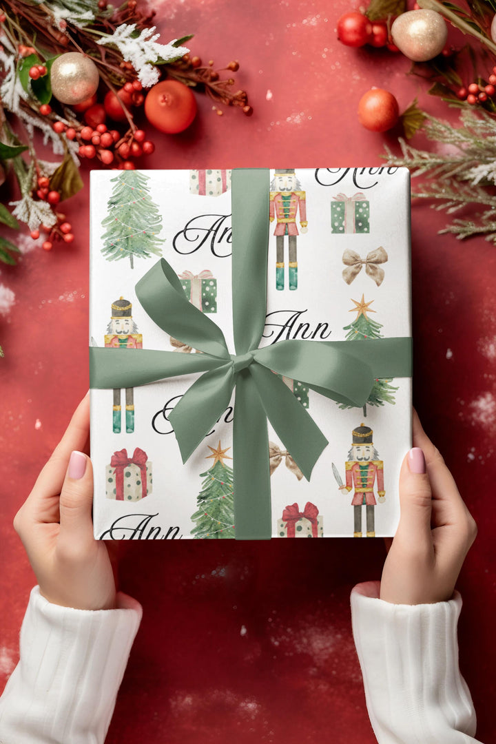 wrapping paper with white background and graphics of a nutcracker, christmas tree, christmas present, bow, and script text with a personalized name