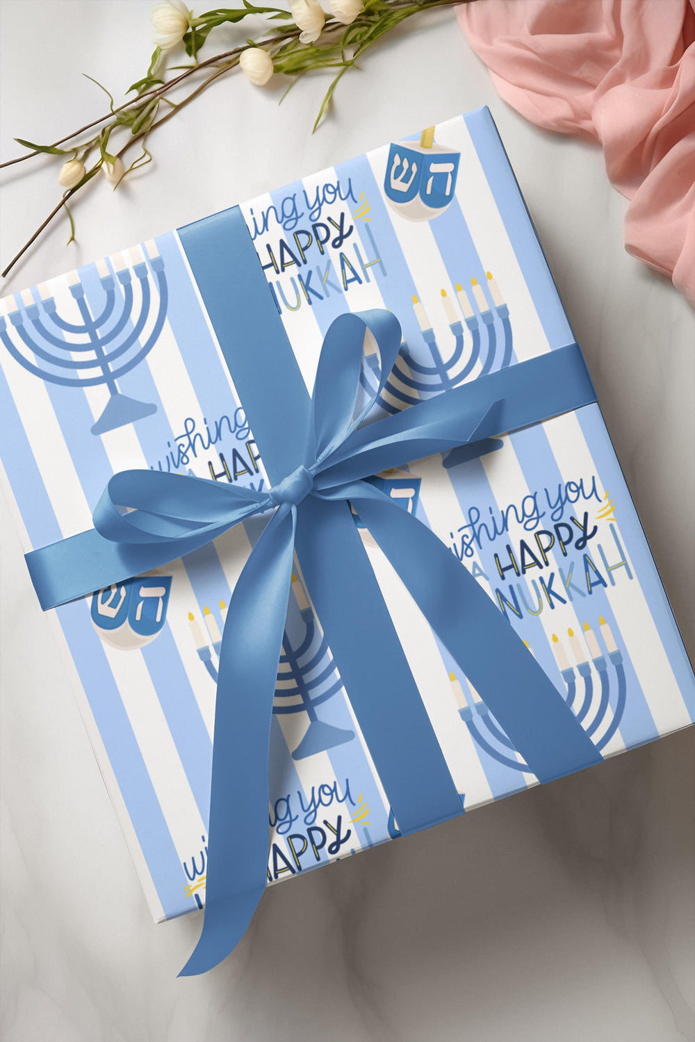 Blue striped wrapping paper with Wishing you a happy Hanukkah text, a graphic of a menorah and dreidel in a varied pattern!