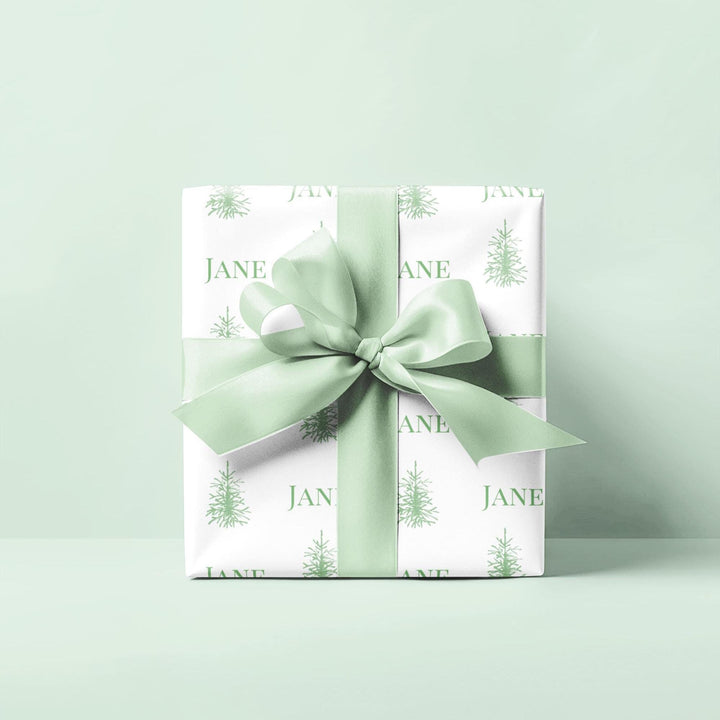 white background with elegant green christmas trees and display font of a personalized name on wrapping paper