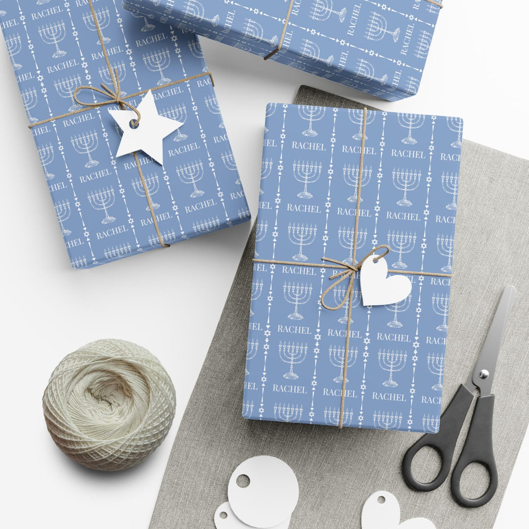 Light blue wrapping paper with white custom name and white menorah graphic and white jewish star graphic