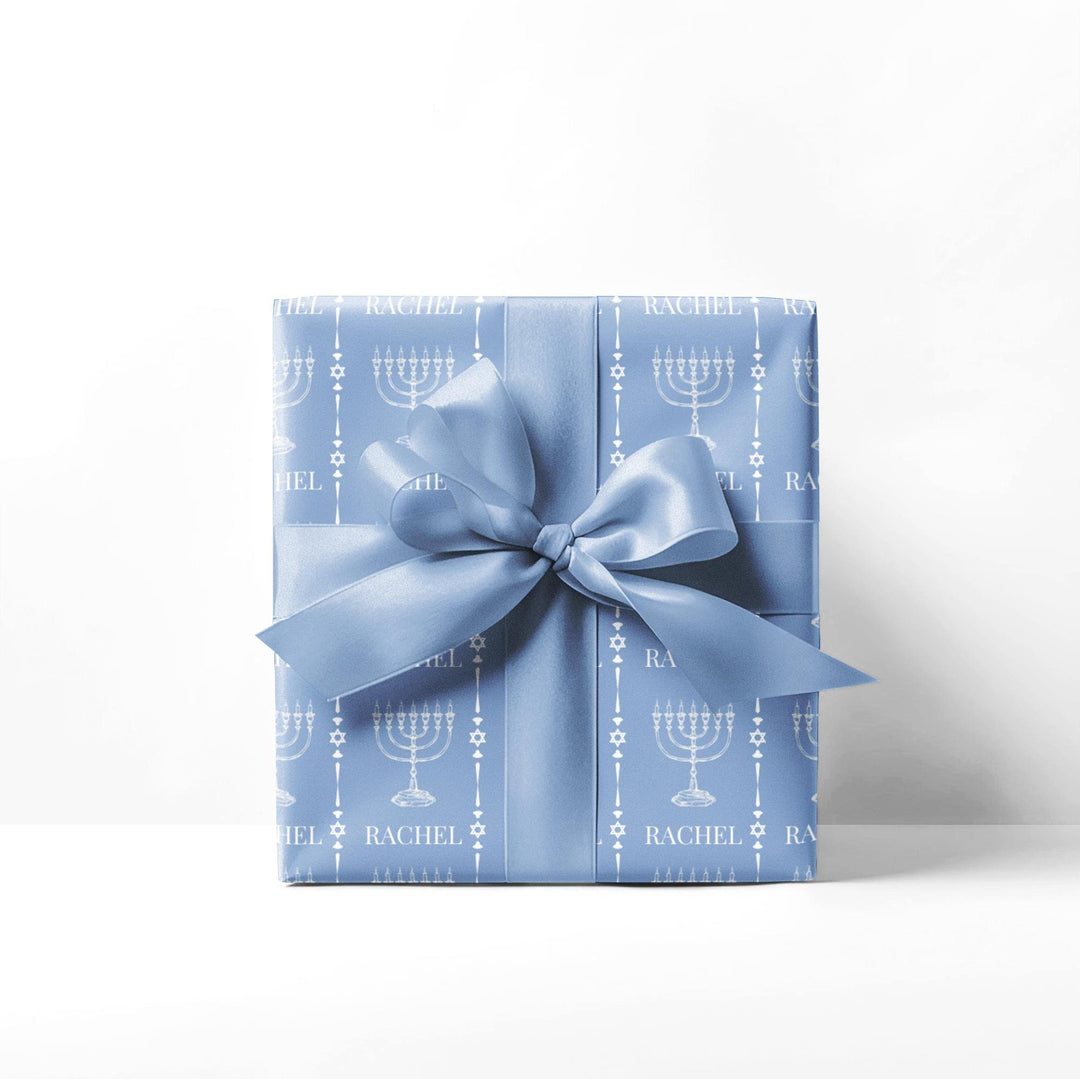 Light blue wrapping paper with white custom name and white menorah graphic and white jewish star graphic