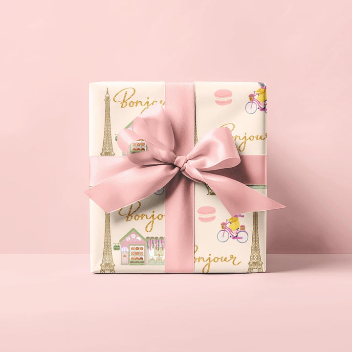 Elegant Paris themed wrapping paper in beige with super cute and fun graphics of a gold Eiffel Tower, adorable French bakery that has florals on the roof of it, &quot;bonjour&quot; text, woman riding her bicycle, pink macaroon