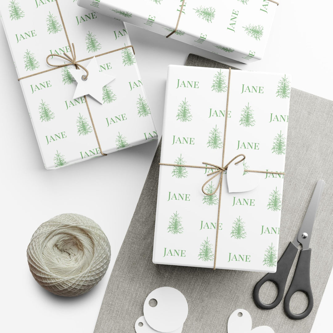 white background with elegant green christmas trees and display font of a personalized name on wrapping paper