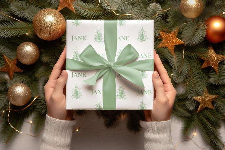 white background with elegant green christmas trees and display font of a personalized name on wrapping paper