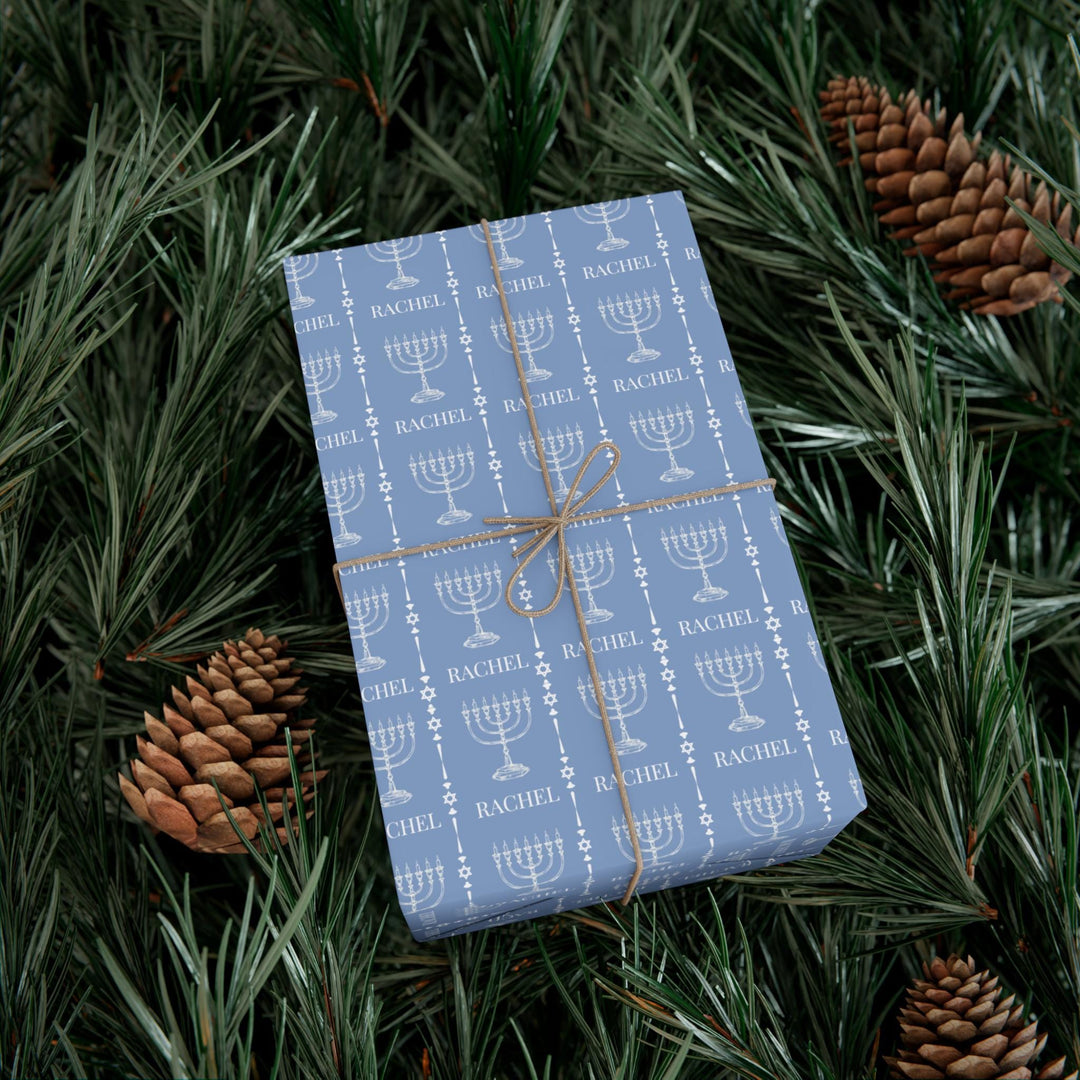 Light blue wrapping paper with white custom name and white menorah graphic and white jewish star graphic