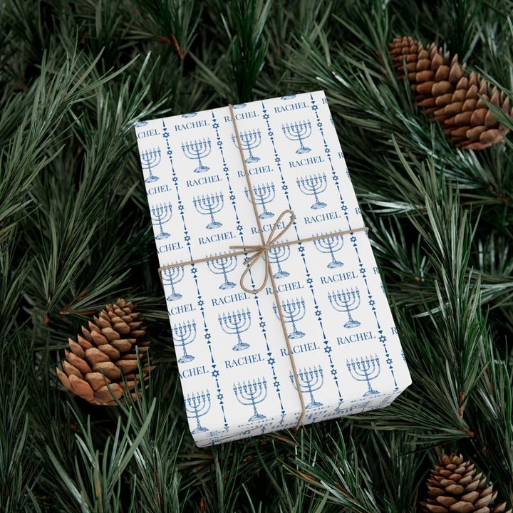 white wrapping paper with blue menorahs and traditional Jewish symbols and personalizable with a name in blue text