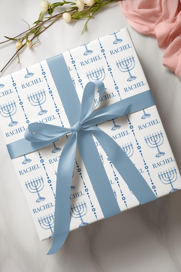 white wrapping paper with blue menorahs and traditional Jewish symbols and personalizable with a name in blue text