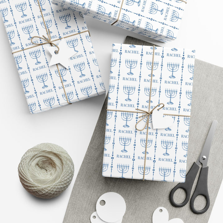 white wrapping paper with blue menorahs and traditional Jewish symbols and personalizable with a name in blue text